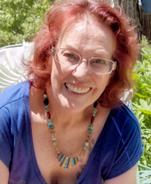 A woman with red hair and glasses smiling for the camera.